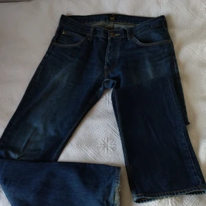 Mörkblå jeans från Lee - Säljer ett par klassiska mörkblå jeans från Lee med fem fickor och snygga slitningar. Jeansen har normal passform och raka ben, perfekt för en avslappnad stil. Gylf av knappar och knapp framtill. W32 L34 (Knox)