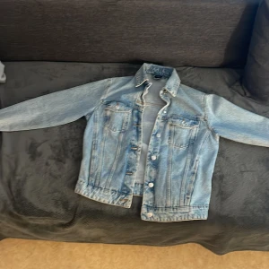 Ljusblå jeansjacka från Vero Moda - Säljer en klassisk ljusblå jeansjacka från Vero Moda i storlek XS. Jackan har långa ärmar, knappar framtill och två bröstfickor med lock. Perfekt att slänga över en hoodie eller t-shirt för en avslappnad look.