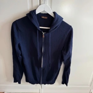 Mörkblå hoodie i merinoull från Stenströms - Mörkblå hoodie i 100% merinoull från stenströms. Tröjan har dragkedja framtill och huva, perfekt för dig som gillar stilrena och bekväma plagg. Storlek är Lagre men sitter som Medium.