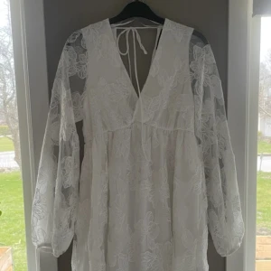 Vit blommig klänning från Gina Tricot - Superfin vit klänning från Gina Tricot med blommigt spetsmönster och transparenta långärmar. Perfekt för sommarens eller studenten. Köpt på vinted så ej använd av mig. Är som ny inga fläckar eller slitningar.