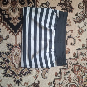 Svartvit randig kortkjol - Säljer en svartvit randig kortkjol med bred svart linning. Kjolen har raka linjer och är i ett slätt material. Perfekt för dig som gillar en stilren och enkel look.