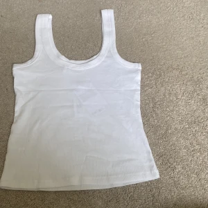 Vit ribbad linnetopp från Monki - Säljer en klassisk vit ribbad linnetopp från Monki. Toppen har breda axelband och rundad halsringning, perfekt för sommaren. Enkel och stilren design som passar till mycket.