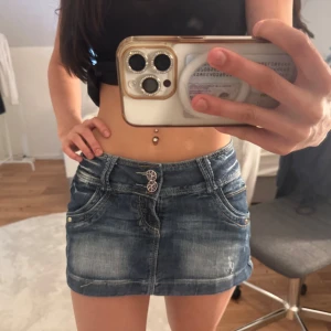 Blå jeanskjol med dekorativa knappar - Säljer en jättesnygg mörkblå kort jeanskjol som är köpt i London. 