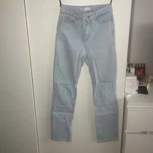 Ljusblå jeans från Zara - Säljer ett par ljusblå jeans från Zara med raka ben. Jeansen har hög midja och stängs med knapp och dragkedja. Perfekta för en avslappnad och stilren look. Finns en liten fläck på ena fickan men inget man tänker på från avstånd.
