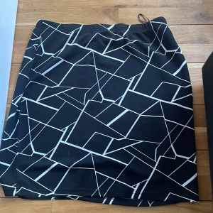 Svart kjol med vitt grafiskt mönster - Säljer en svart kjol med vitt grafiskt, geometriskt mönster. Kjolen har en rak passform och resår i midjan. Perfekt för dig som gillar en modern och stilren look.