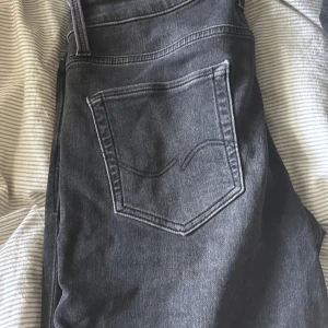 Svarta slim jeans från Jack & Jones - Säljer ett par svarta slim fit jeans från Jack & Jones, modell Glenn. Jeansen har klassisk femficksdesign och diskret bakficka med broderad detalj. Perfekta för dig som gillar en smalare passform och stilren look.