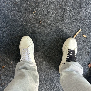 Vita sneakers från 1998. - Säljer ett par vita sneakers från märket 1998. Skorna har klassisk design med rund tå, platt sula och snörning. Ena skon har svarta skosnören och den andra vita, vilket ger en unik look. Perfekta för dig som gillar stilrena och enkla sneakers.