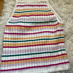 Randig ribbad linnetopp från H&M - Säljer en ribbad linnetopp från H&M med färgglada ränder i rosa, orange, grön och lila på vit botten. Toppen är ärmlös och har en mjuk, stretchig känsla. Perfekt för varma dagar!
