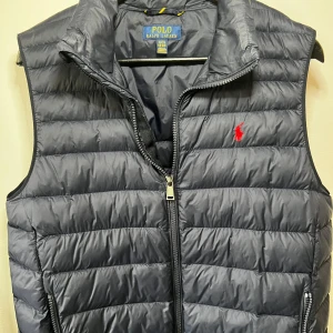 Mörkblå dunväst från Polo Ralph Lauren - Snygg mörkblå dunväst från Polo Ralph Lauren med klassisk quiltad design och dragkedja. Barn storlek XL men passar S/XS. Nypris 2200kr men säljer för 600kr. Skick 9,5/10 näst intill ny.