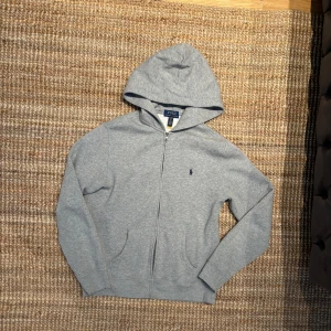 Grå hoodie från Polo Ralph Lauren - Säljer en grå hoodie från Polo Ralph Lauren med dragkedja och huva. 