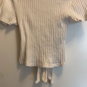 Vit ribbad knyt-topp - Säljer en stilren vit ribbad topp med korta ärmar och knytning i midjan. Perfekt för en avslappnad look den är i ny skick från New Yorker I storlek XS.