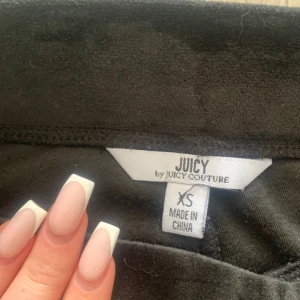 Svarta byxor från Juicy Couture - Snygga svarta byxor från Juicy Couture i mjukt material. Byxorna har en broderad krona på fickan och en avslappnad passform. Perfekta för en bekväm och stilren look.