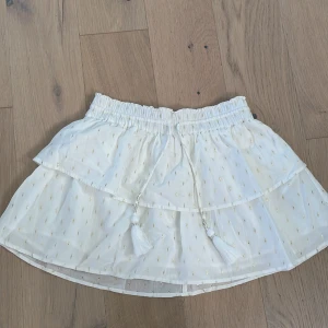 Vit kortkjol med volangdetaljer - Söt vit kortkjol med volang och små guldiga detaljer