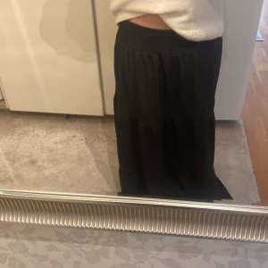 Svart maxi kjol - Säljer en stilren svart maxi kjol med en  elastisk midja. Kjolen har en luftig passform och är perfekt för både vardag och festliga tillfällen. Passar utmärkt till en stickad tröja eller en elegant blus. Prislappen frf på/ oanvänd. Storlek S men passar som M