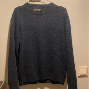 Mörkblå stickad tröja från Oscar Jacobson - Säljer en stilren mörkblå tröja från Oscar Jacobson, tillverkad i Yorkshire Tweed av Moon. Tröjan har långa ärmar och ribbade muddar vid ärmslut och nederkant. Perfekt för kyligare dagar.