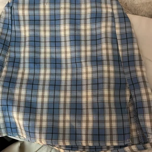 Blå och vit rutig kjol - Snygg blå och vit rutig kjol med en klassisk design. Kjolen har en kort längd och en bekväm passform med elastisk midja. Perfekt för en stilren look.