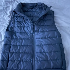 Blå dunväst från H&M - Säljer en stilren blå dunväst från H&M. Västen har en dragkedja framtill och är perfekt för lager-på-lager under kyligare dagar. Den quiltade designen ger en modern look. Modellen är 180 60kg sitter litet på mig🙌