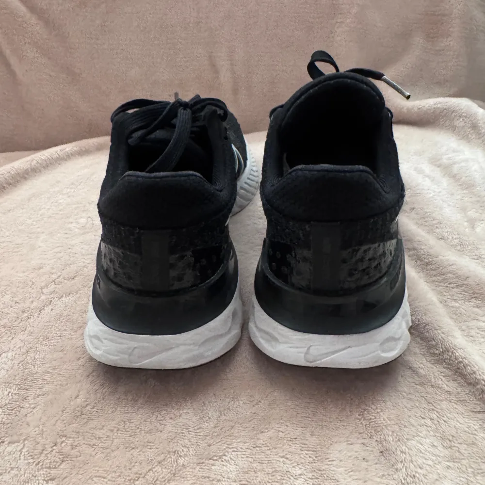 Snygga svarta Nike sneakers med vit sula och klassisk swoosh-logga i vitt. Skorna har en stickad ovandel och snörning för en bekväm passform. Perfekta för både träning och vardag. Oups har tappat bort sulorna till skorna. Kengät.