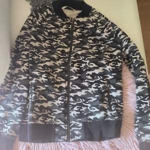 Säljer en snygg bomberkofta i camouflage från House of Lola. Jackan har en dragkedja framtill och är långärmad med ribbade muddar. Perfekt för en cool och avslappnad stil.