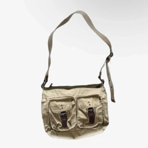 Beige axelväska med spännen - Säljer en beige slitstark axelväska med justerbar axelrem. Väskan har två framfickor med snygga spännen och en dragkedja upptill. Perfekt för vardagsbruk och rymmer det mesta du behöver ha med dig.