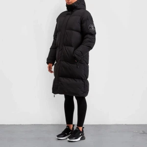 Svart lång dunjacka - Säljer en stilren svart lång dunjacka från Svart lång dunjackaZavetti . Jackan har en hög krage och dragkedja framtill. Perfekt för kalla dagar med sin varma och skyddande design. Den har långa ärmar och en diskret logga på ärmen. har använt några gånger men ser som ny ut!