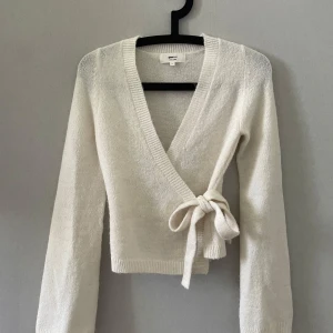 Vit omlottkofta från Gina Tricot - Säljer en stilren vit omlottkofta från Gina Tricot i ullblandning. Koftan har långa ärmar och en knytning i sidan för en elegant look. Perfekt för kyligare dagar!