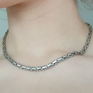 Silverfärgat halsband med mönster - Snyggt och stilrent halsband i silverfärg med ett intrikat mönster. Perfekt för att ge en elegant touch till din outfit. Halsbandet har en krokstängning som gör det enkelt att ta på och av.