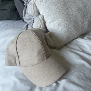 Beige keps - Snygg beige keps i bomullsmaterial. Perfekt för en avslappnad stil och passar till många olika outfits. Kepsen har en klassisk design med justerbar rem baktill.