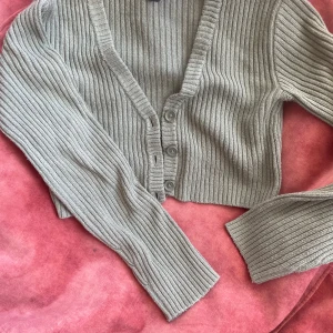 Grön ribbad kofta från Gina Tricot - Snygg grön ribbad kofta från Gina Tricot med v-ringning och knappar framtill. Perfekt för lager-på-lager och ger en stilren look. Passar bra till både jeans och kjol. 