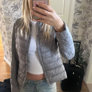 Grå dunjacka från Uniqlo - Säljer en stilren grå dunjacka från Uniqlo. Jackan har en lätt och bekväm passform med långa ärmar