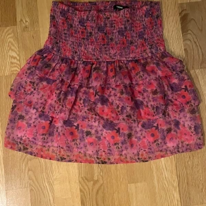 Blommig kjol från BikBok - Säljer en färgglad blommig kjol från BikBok i storlek S. Kjolen har volanger och ett elastiskt midjeband för en bekväm passform. Perfekt för sommarens äventyr!