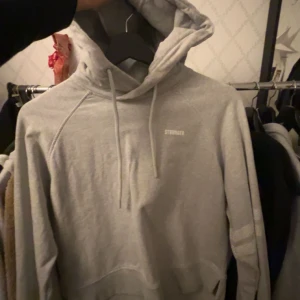 Grå hoodie från Stronger - Säljer en stilren grå hoodie från Stronger i storlek XS. Den är tillverkad av mjuk bomull med en liten andel elastan för extra komfort. Hoodien har en klassisk design med dragsko i huvan och en diskret logga på bröstet. Skriv för fler bilder, köparen står för frakten!🤍