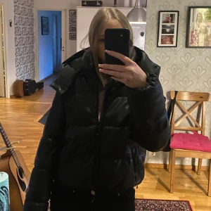Svart pufferjacka från NA-KD - Säljer denna svarta pufferjacka från NA-KD. Jackan har en dragkedja framtill och en stor huva för extra värme. Den sitter jättefint men tyvärr har en knapp från fickan lossnat. Utöver det, jättebra skick! Den är i storlek 36💓 pris kan diskuteras!