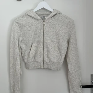 Grå croppad hoodie från H&M Divided - Säljer en grå croppad hoodie från H&M Divided. Den har en dragkedja framtill och en mysig huva. Perfekt för en avslappnad stil. 