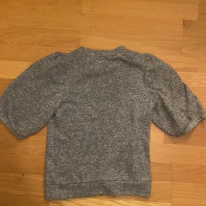 Grå tröja stickad - Säljer en trendig grå stickad tshirt. Perfekt för en avslappnad look. Tröjan har en rund halsringning och är tillverkad i ett mjukt och bekvämt material.