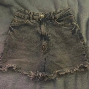 Svarta jeansshorts från Divided - Snygga svarta jeansshorts från Divided med fransiga kanter och hög midja. Perfekta för en avslappnad stil. De har klassiska fem fickor och en knappgylf. Perfekta för sommardagar!