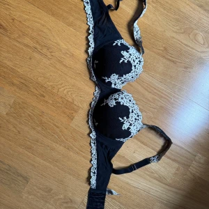 Svart intimissimi spets-bh med broderade detaljer - Säljer en elegant svart intimissimi bh med vacker spets och broderade blommor i vitt. Bh:n har justerbara axelband och en klassisk knäppning bak. Perfekt för att känna sig extra fin under kläderna. 🌸