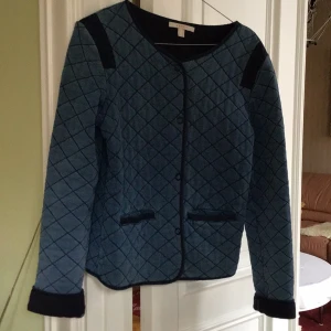 Blå quiltad jacka från Esprit - Säljer en snygg blå quiltad jacka från Esprit. Jackan har ett rutigt mönster och svarta detaljer vid axlar och ärmslut. Den är långärmad och har en stilren design med rund halsringning.