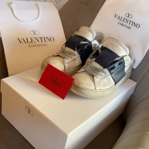 Valentino Garavani sneakers - Snygga Valentino Garavani sneakers i vitt med mörkblåa  detaljer. Skorna har en unik design med breda mörkblåa  band över snörningen. Perfekta för dig som vill ha en stilren och modern look.