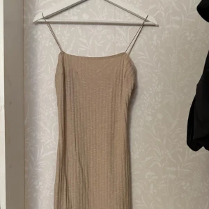 Beige ribbad klänning från NLY One - Snygg beige ribbad klänning från NLY One med smala axelband och en matchande långärmad kofta. Perfekt för en stilren look. Klänningen har en enkel och elegant design som passar till många tillfällen.