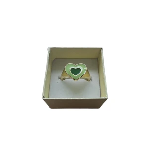 Guldfärgad ring med grönt hjärta - Snygg guldfärgad ring med ett grönt hjärta i mitten. Perfekt för att ge en färgklick till din outfit. Hjärtat ger en söt och lekfull touch. Okänt Material, US 8 eller 18.1 mm