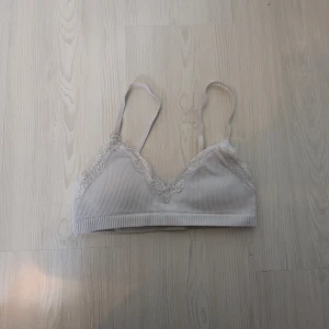 Vit ribbad bralette  med spetsdetaljer - Säljer en söt vit ribbad bralette med spetsdetaljer längs kanterna. Toppen har justerbara axelband och en mjuk, bekväm passform. Är storlek xs men sitter som en xxs