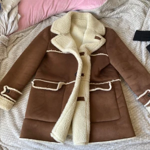 Brun jacka med teddyfoder från Zara Man - Säljer en snygg oanvänd XL jacka från ZARA. Jackan har långa ärmar och knappar framtill. Perfekt för kyliga dagar med sin varma och stiliga design.