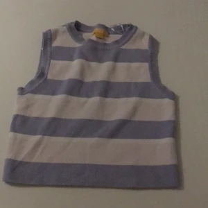 Randig ärmlös topp - Säljer en söt ärmlös topp med breda ränder i lila, rosa och vitt. Perfekt för varma dagar eller som ett lager under en jacka. Den har en rund halsringning och är gjord i ett mjukt material.
