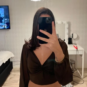 Brun v-ringad croppad blus - Snygg brun blus med v-ringning och knytning framtill. Den är croppad och har långa ärmar som ger en elegant look. Perfekt för en kväll ute eller en speciell tillställning.