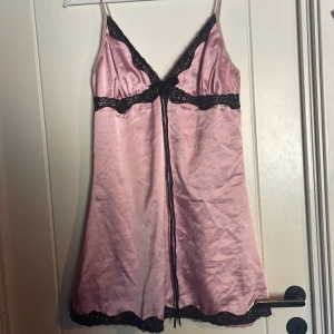 Rosa nattlinne från LivCo Corsetti - Säljer ett elegant rosa nattlinne från LivCo Corsetti med svarta spetsdetaljer. Klänningen har smala axelband och en dekorativ rosett framtill. Perfekt för en speciell kväll! 💖