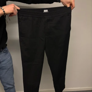 Svarta byxor från Filippa K - Snygga svarta byxor från Filippa K med elastisk midja för extra komfort. Perfekta för en stilren look. Byxorna har en klassisk design som passar till många olika tillfällen.