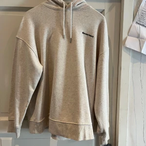 Beige hoodie från Helena Christensen x H&M - Säljer en snygg beige hoodie från Helena Christensen x H&M med texten 'discover beauty' på bröstet. Baksidan har ett stort blommigt tryck i lila och blå toner. Tröjans stil är ”oversized” så passar även en M/L-person. I mkt fint skick, från djur/rökfritt hem. OBS! Fri frakt!