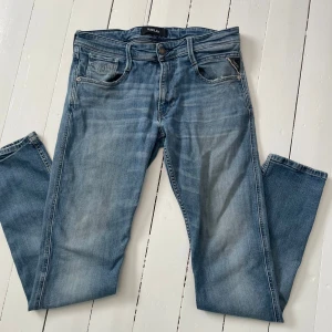 Replay anbass  - Snygga blå jeans från Replay med klassisk femficksdesign och knappgylf. De har en normal passform och är perfekta för en avslappnad stil. Märkeslogga på baksidan av midjan ger en extra touch. Finns lite slitage som ni ser på den sista bilden!
