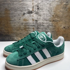 Adidas Campus (oanvända) - Snygga gröna Adidas Campus sneakers i mocka med de klassiska vita tre ränderna på sidan. Skorna är helt nya och oanvända.Nypris: 1400kr, vårt pris: 799kr.        Storlek 42,5. Dessa skor kommer ge din stil ett lyft💯(pris kan diskuteras)